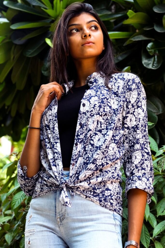 Home Confident woman posing in stylish floral shirt and jeans against lush green background.