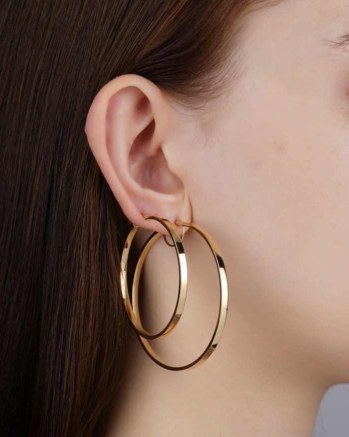 Home Elegant close-up of a woman's ear adorned with large gold hoop earrings, showcasing jewelry fashion.