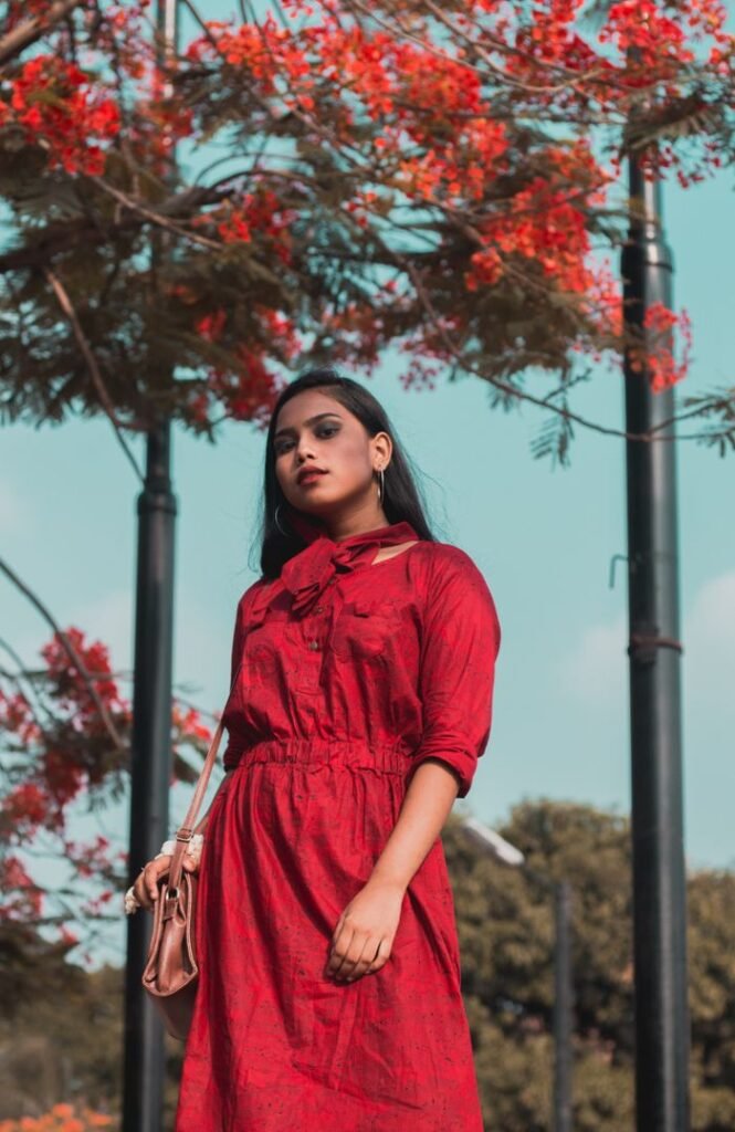 Home Fashionable woman posing in a red dress outdoors in a park setting.