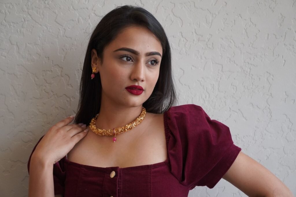 Home Stunning portrait of a woman with dark hair, wearing a burgundy dress and gold necklace.