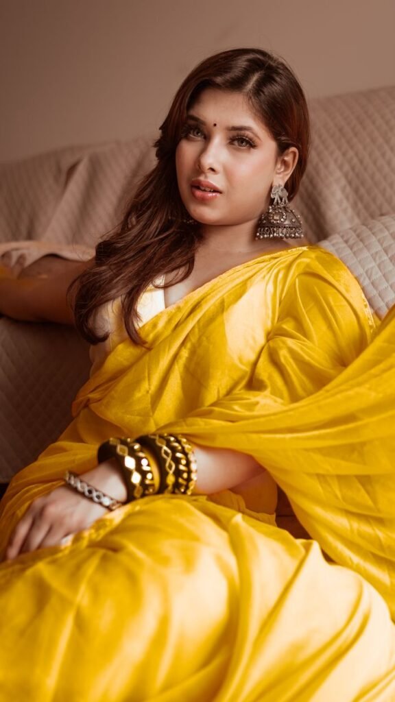 About Elegant woman in a vibrant yellow saree with traditional jewelry, relaxing indoors.