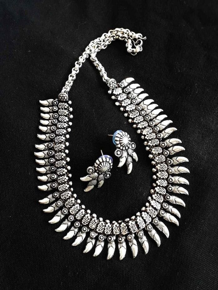Home Intricate silver necklace and earrings displayed on a black background.